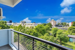 Varanda com grades de metal e vista para um horizonte urbano com edifícios e áreas verdes.