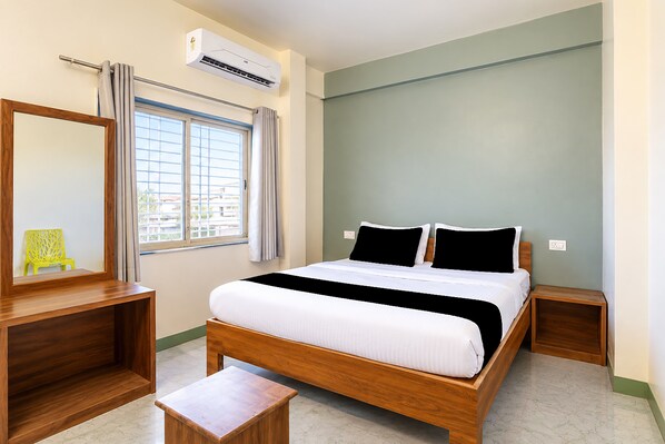A bedroom with a bed, a wooden nightstand, a small wooden table, a mirror, and an air conditioning unit. - Hotel O Aura Inn (Chhatrapati Sambhajinagar)