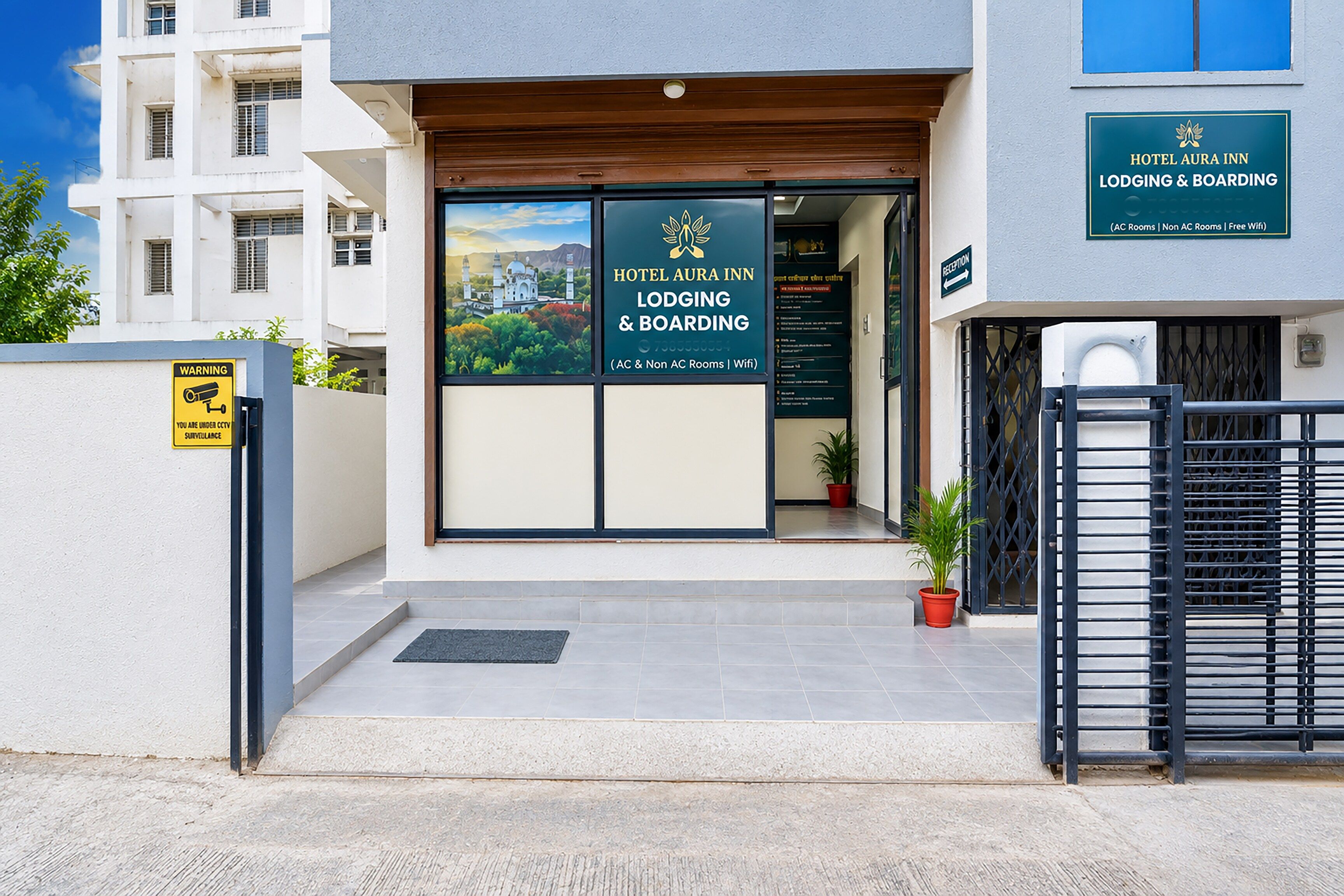 A hotel entrance with a sign for Hotel Aura Inn, indicating AC and Non-AC rooms, and WiFi availability.