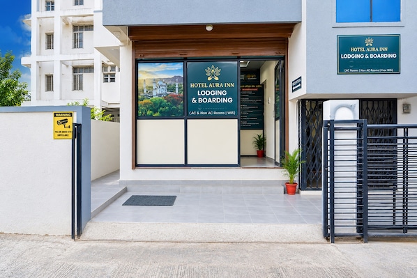 Entrada de hotel com placa indicando Hotel Aura Inn, com quartos com e sem ar condicionado, e disponibilidade de WiFi.