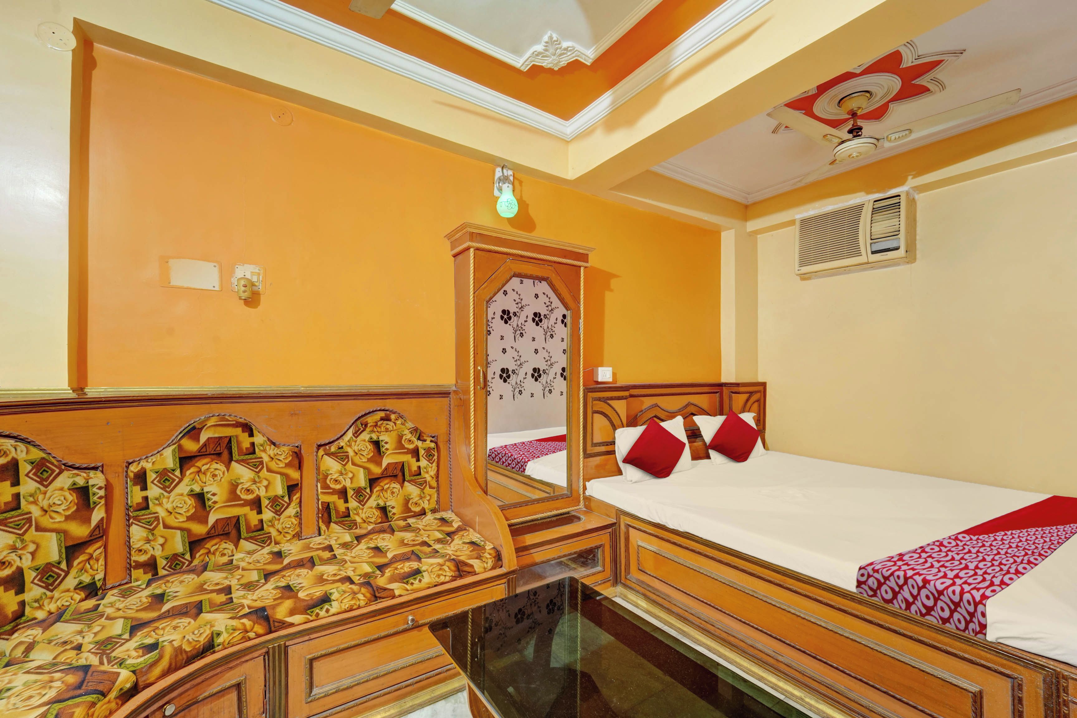 A hotel room with a bed, a mirror, a wardrobe, and a ceiling with decorative elements.