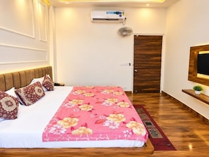 A bedroom with a bed, a wooden floor, a wall-mounted air conditioner, a door, and a small plant on a shelf. - Hotel O Grand Park (Amritsar)