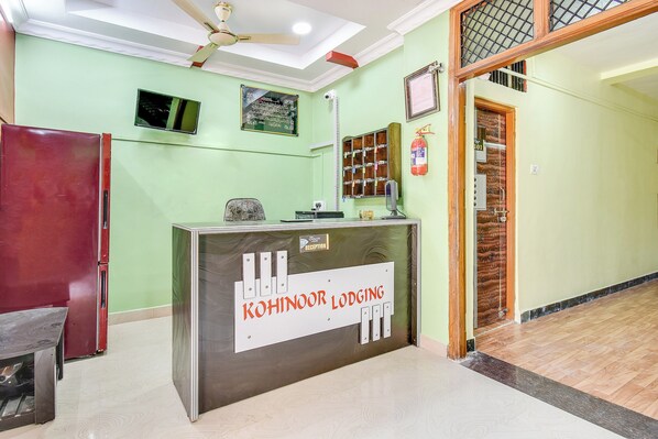 A reception desk with a sign for 'Kohinoor Lodging' in a room with green walls and a wooden floor.