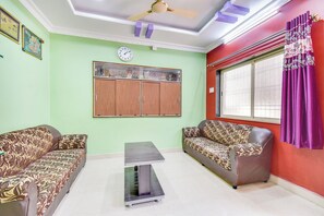 Una habitación con dos sofás, una mesita, un ventilador de techo, un reloj y una ventana con cortinas.