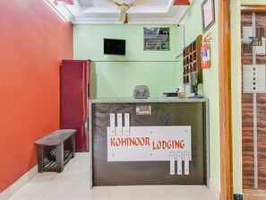 Una recepción con un cartel de Kohinoor Lodging, un extintor y un televisor montado en la pared.