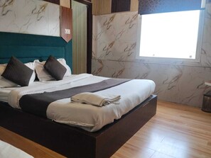 Una cama bien hecha con almohadas y una colcha, piso de madera y ventana con vistas.