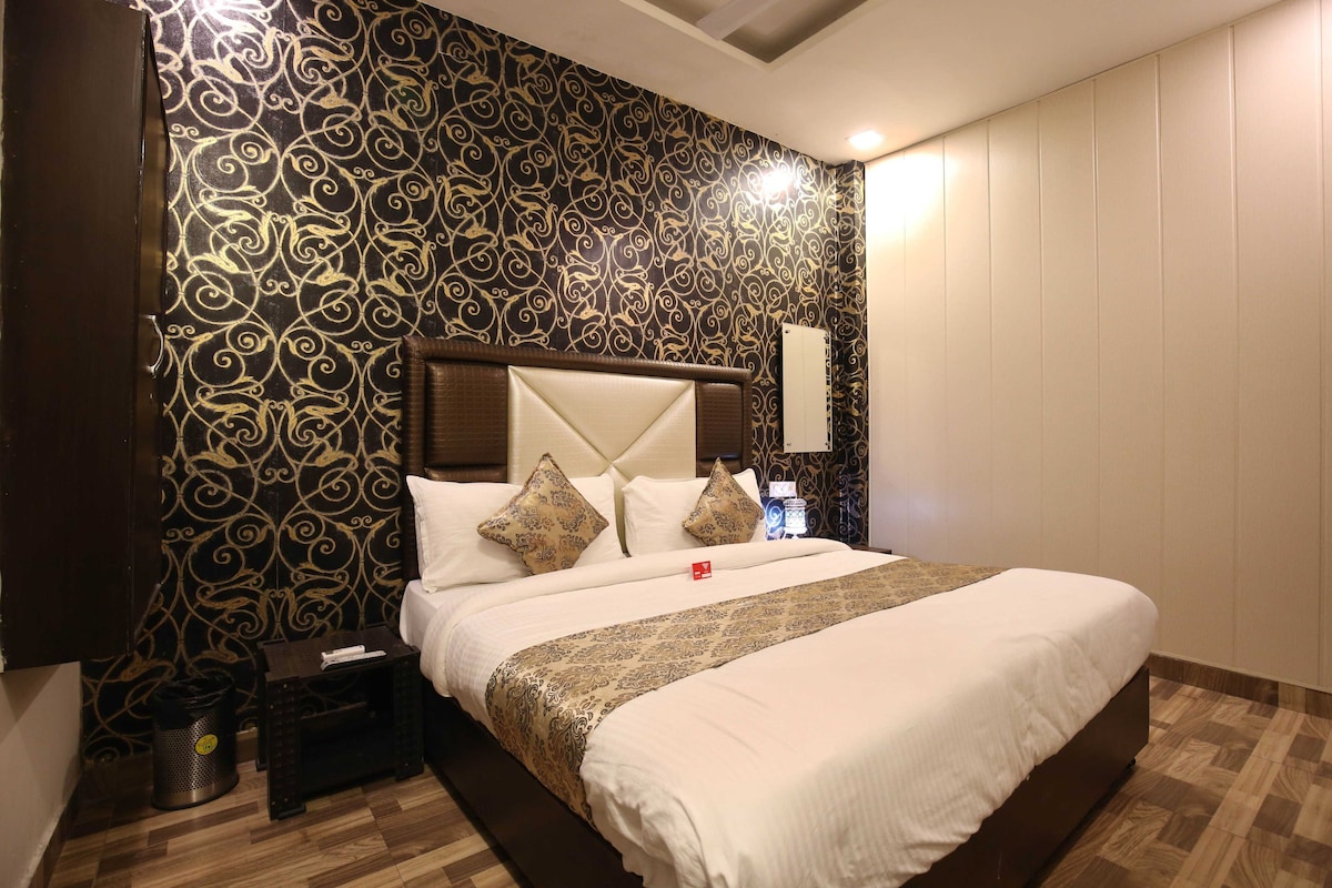 A hotel room with a large bed, a nightstand, a trash bin, and a wall with a decorative pattern.