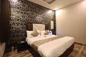 A hotel room with a large bed, a nightstand, a trash bin, and a wall with a decorative pattern. - Hotel O chohan residency (Amritsar)