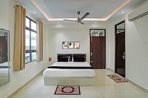 A modern bedroom with a large bed, a ceiling fan, and a window with curtains. - Townhouse Hotel SRV inn (Lucknow)