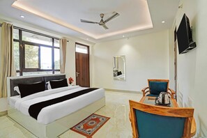 A hotel room with a bed, a desk with a chair, a ceiling fan, a TV mounted on the wall, and a window with curtains. - Townhouse Hotel SRV inn (Lucknow)