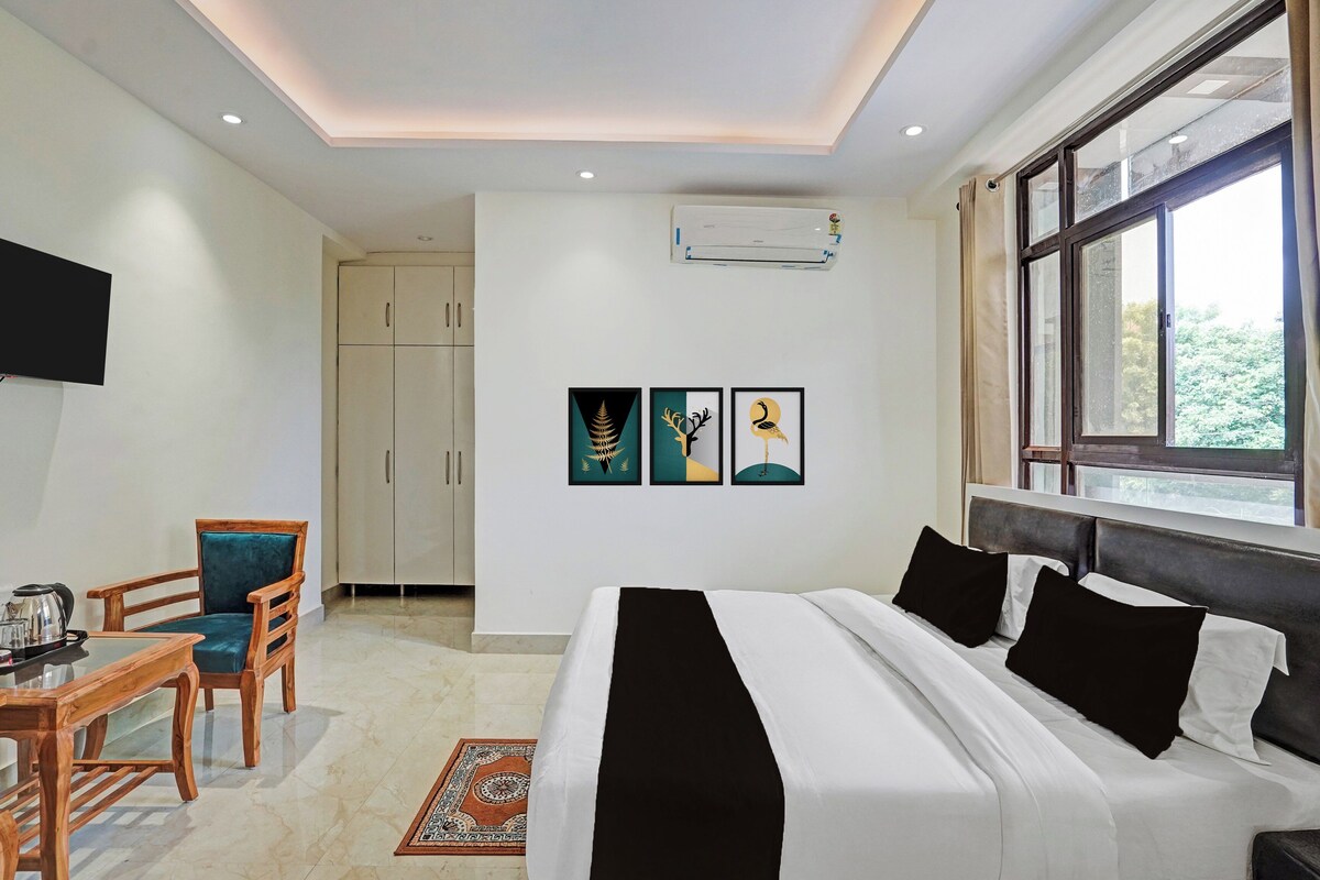 A hotel room with a bed, a desk with a chair, a television, and artwork on the wall.