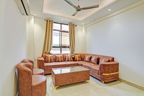 A spacious living room with a large L-shaped sectional sofa, a glass coffee table, and a ceiling fan. - Townhouse Hotel SRV inn (Lucknow)