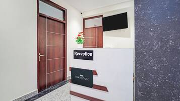 A reception area with a wooden door, a reception desk, a potted plant, and a flat-screen TV mounted on the wall.