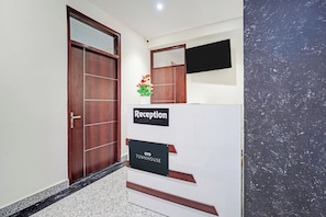 A reception area with a wooden door, a reception desk, a potted plant, and a flat-screen TV mounted on the wall. - Townhouse Hotel SRV inn (Lucknow)
