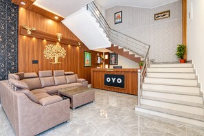 A hotel lobby with a reception desk, a staircase, a sectional sofa, and a decorative tree wall. - Hotel O Aurivique hotels and Banquets (Lucknow)