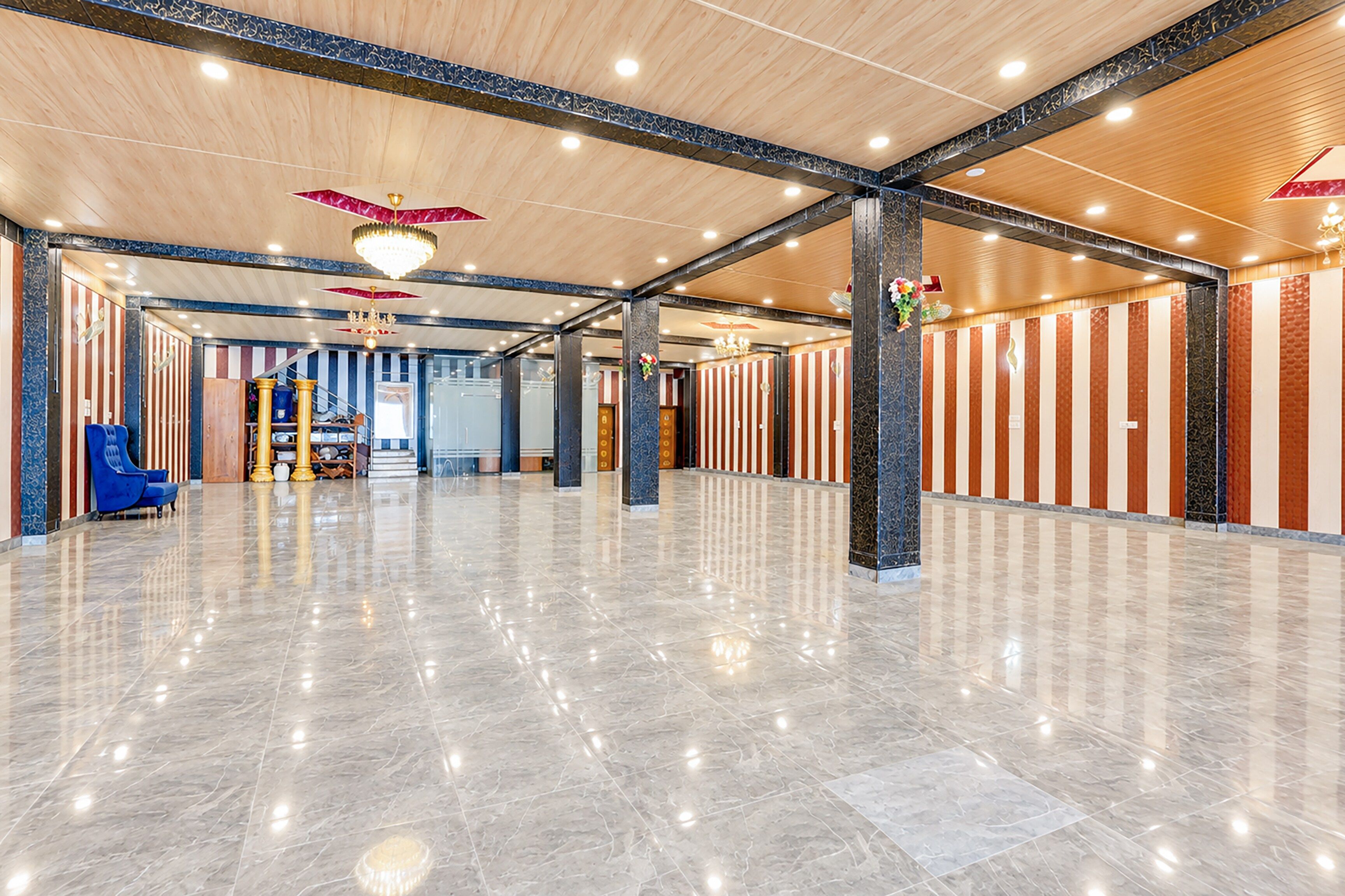 Un vestíbulo amplio con piso de mármol pulido, techos altos con vigas a la vista y una escalera central.