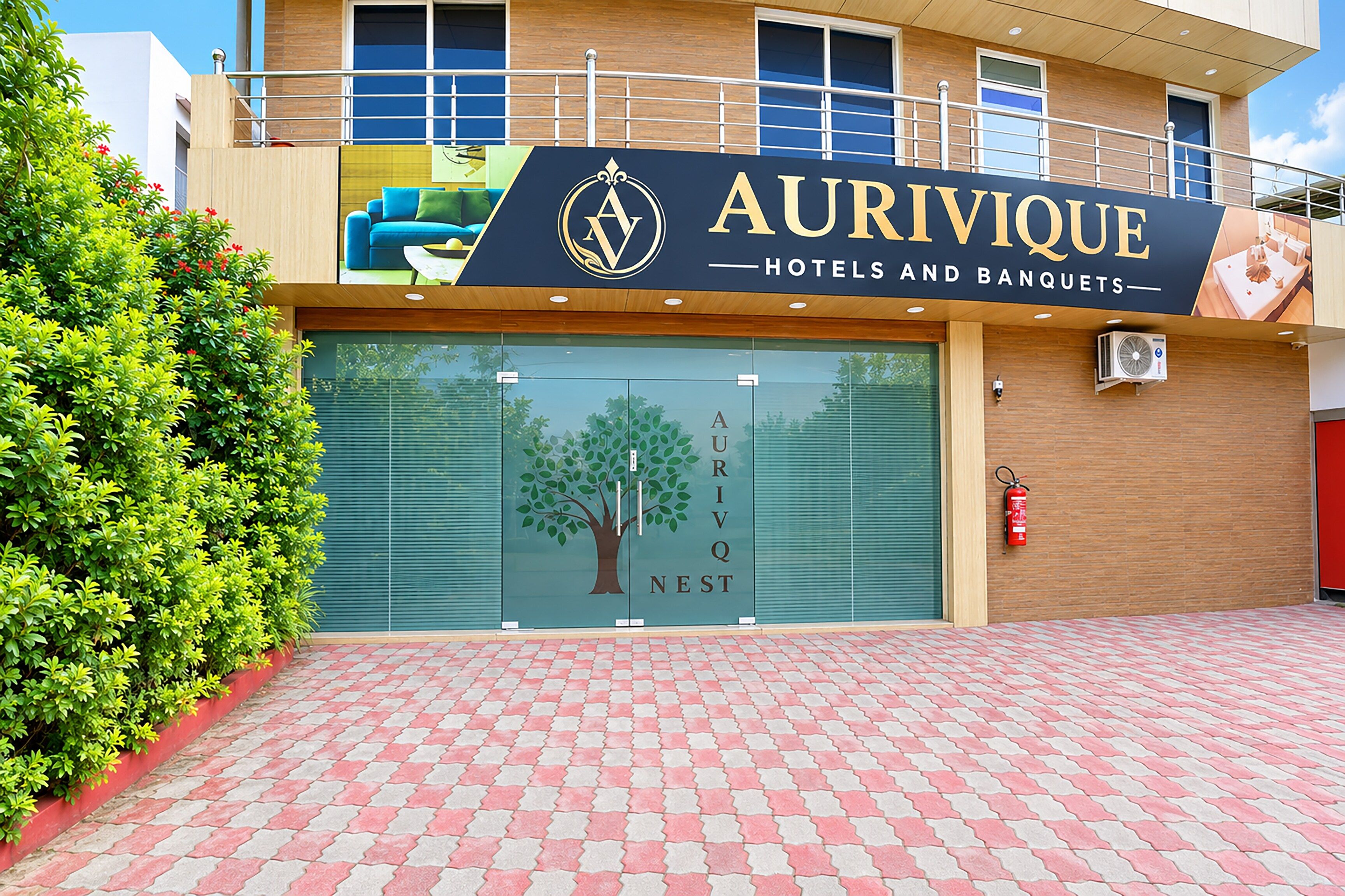Entrada de un hotel con un letrero que dice 'AURIVIQUE HOTELS AND BANQUETS' y un gráfico de árbol en la puerta.