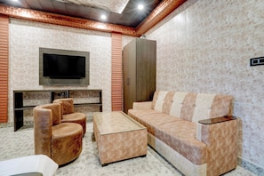 A modern living room with a flat-screen TV, a sofa, two armchairs, and a coffee table. - Hotel O Aurivique hotels and Banquets (Lucknow)