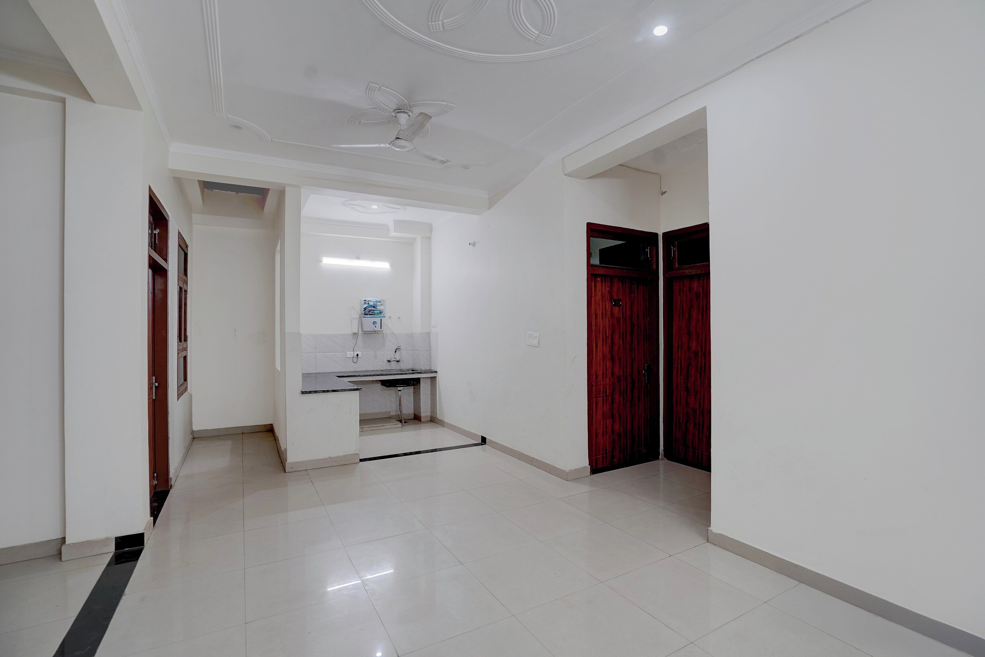 A hallway with a white ceiling, a ceiling fan, a sink with a mirror, and a red door.