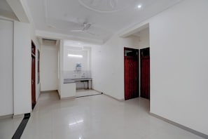 A hallway with a white ceiling, a ceiling fan, a sink with a mirror, and a red door. - Hotel O The Sukoon House (Lucknow)