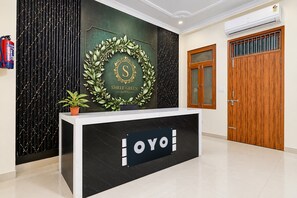 A hotel reception desk with a sign that reads 'Shree Green Hotel' and a logo with a 'S' inside a laurel wreath. - Hotel O The Sukoon House (Lucknow)