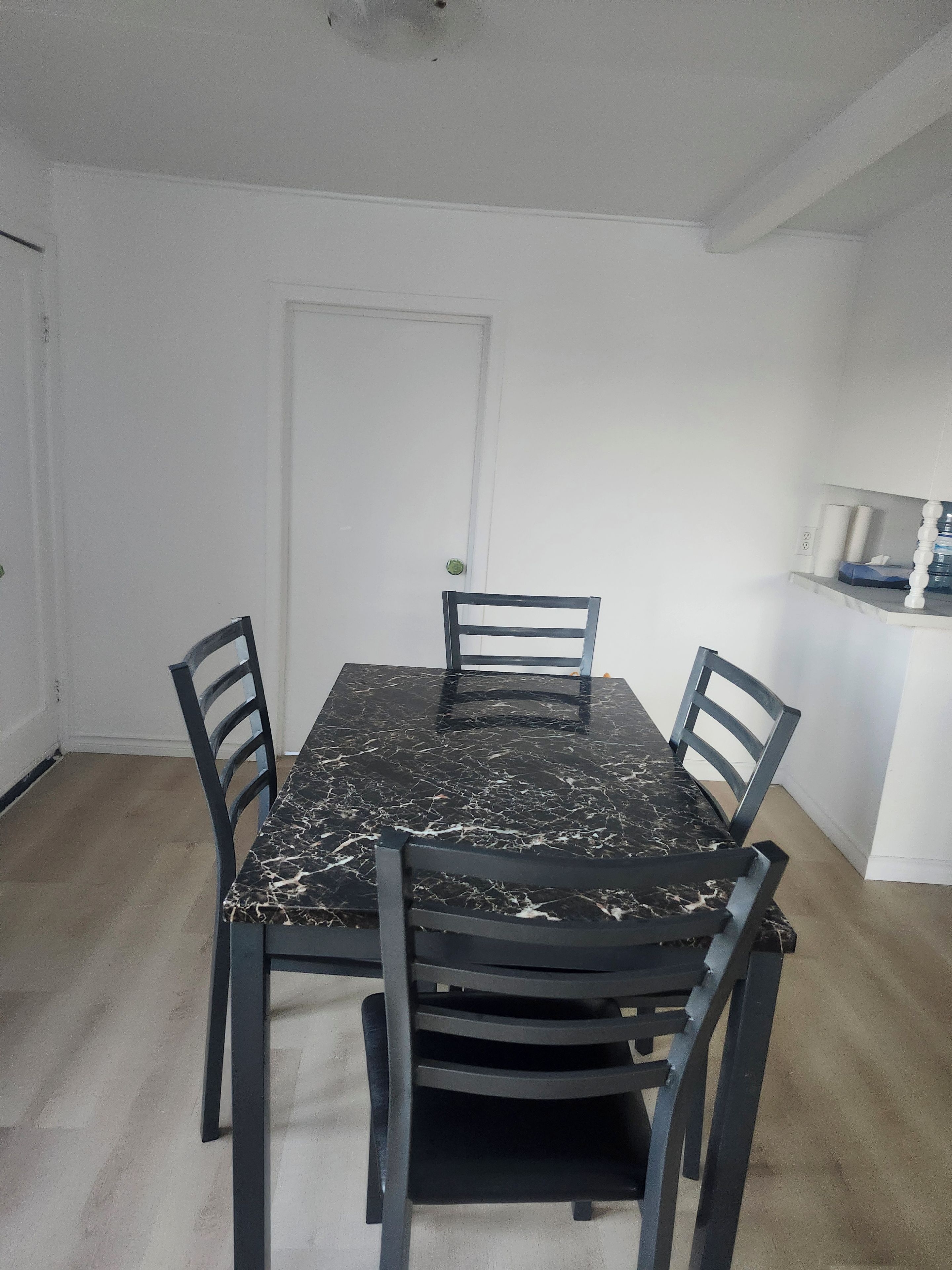 A dining area with a marble table and four chairs, a white door, and a shelf with items.