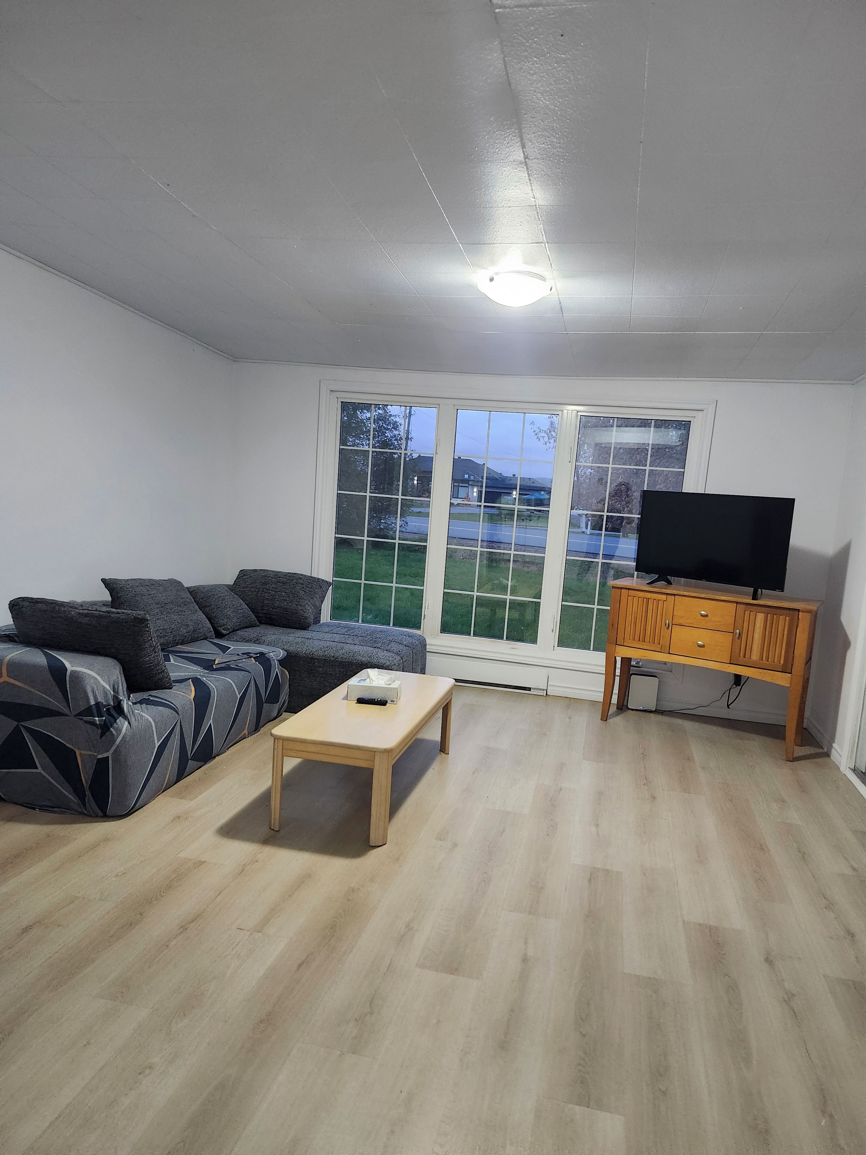 Una sala de estar con un sofá, una mesa de centro, un mueble para televisor y vistas amplias a través de grandes ventanales.