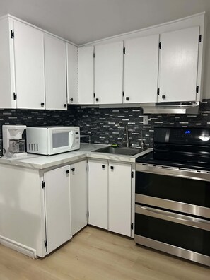 A kitchen with white cabinets, a microwave, a sink, and a stainless steel oven.