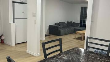A dining area with a marble table and chairs, a kitchen with white cabinets, and a living room with a grey sofa.