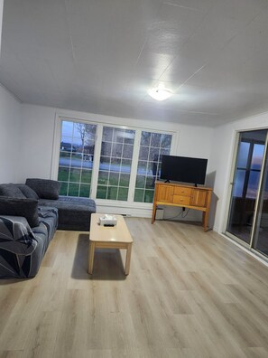 A living room with a sofa, a coffee table, a TV on a stand, and a sliding glass door.