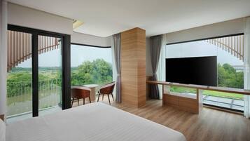 A modern hotel room with a large bed, a flat-screen TV, a desk, and a balcony with a view of greenery.