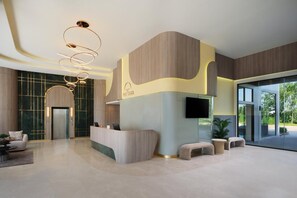 Una zona d'entrada moderna amb un taulell de recepció corbat, un televisor de pantalla plana i una gran porta de vidre que dona a una zona exterior.