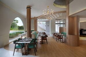 Un restaurant modern amb una taula de menjador llarga, cadires tapissades de verd i un penjador.