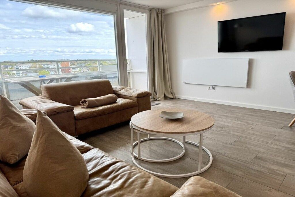 A modern living room with a sofa, a round coffee table, and a flat-screen TV mounted on the wall.