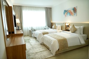 Une chambre d’hôtel avec deux lits, un bureau, une chaise, une grande fenêtre avec des rideaux et un tableau au mur.