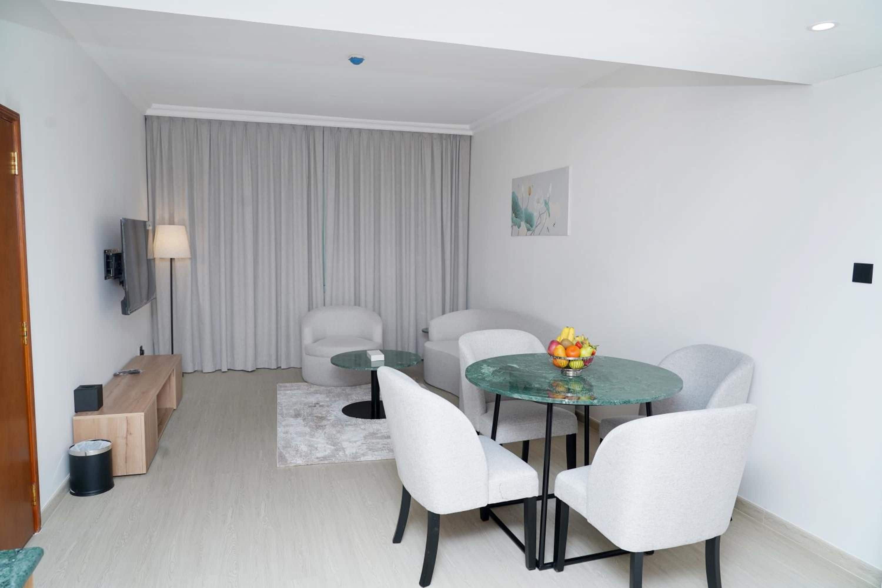 Una habitación de hotel moderna con zona de comedor, sofá, televisor y un cuadro en la pared.