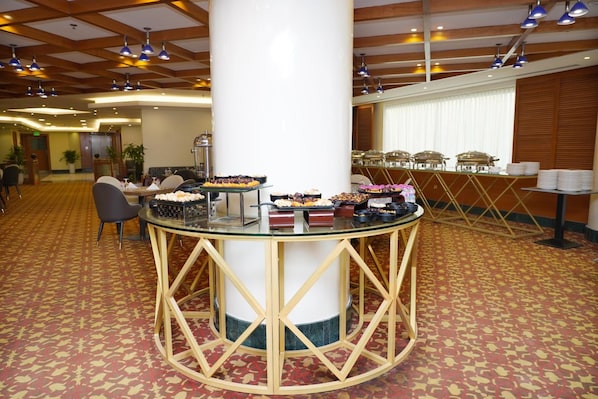 Un buffet avec différentes sortes de plats présentés sur des tables, un pilier central et un sol recouvert d’un tapis à motifs.