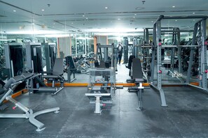 Une salle de sport équipée de divers appareils d’exercice, de miroirs, et où une personne utilise une machine.