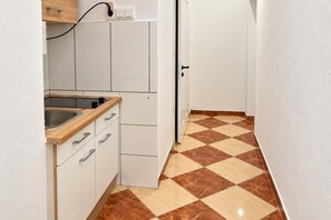 A narrow kitchen with a sink, cabinets, and a checkered floor. - Your Vienna Encore 1BR near Stadthalle (Vienna)