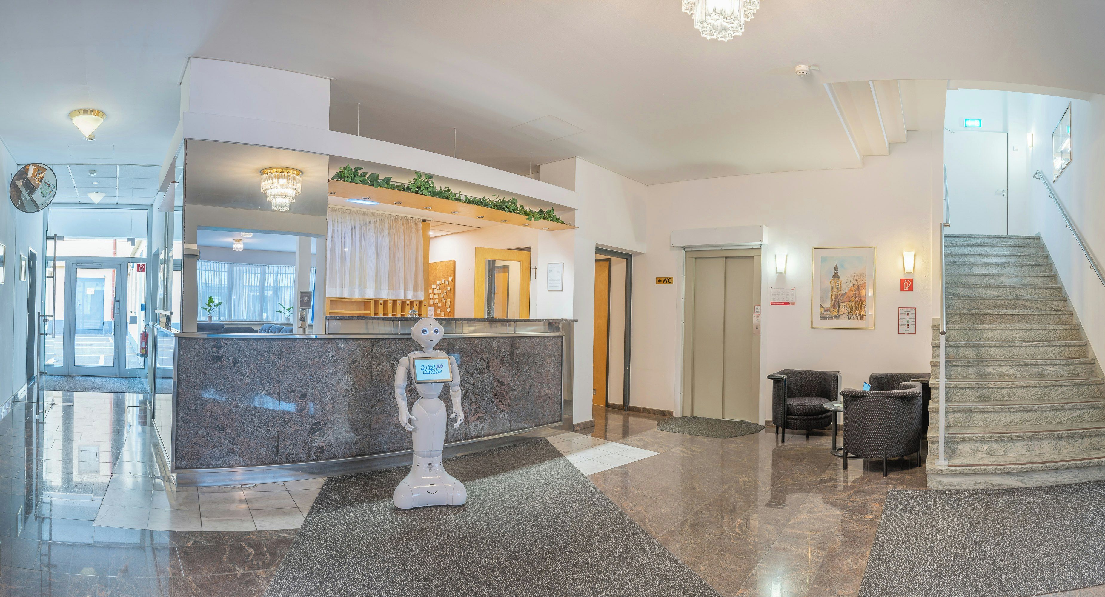 A hotel lobby with a reception desk, a robot, a staircase, and a reception area with a plant.