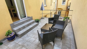 Un patio con una mesa y sillas, escalones que llevan a una puerta y plantas en macetas.