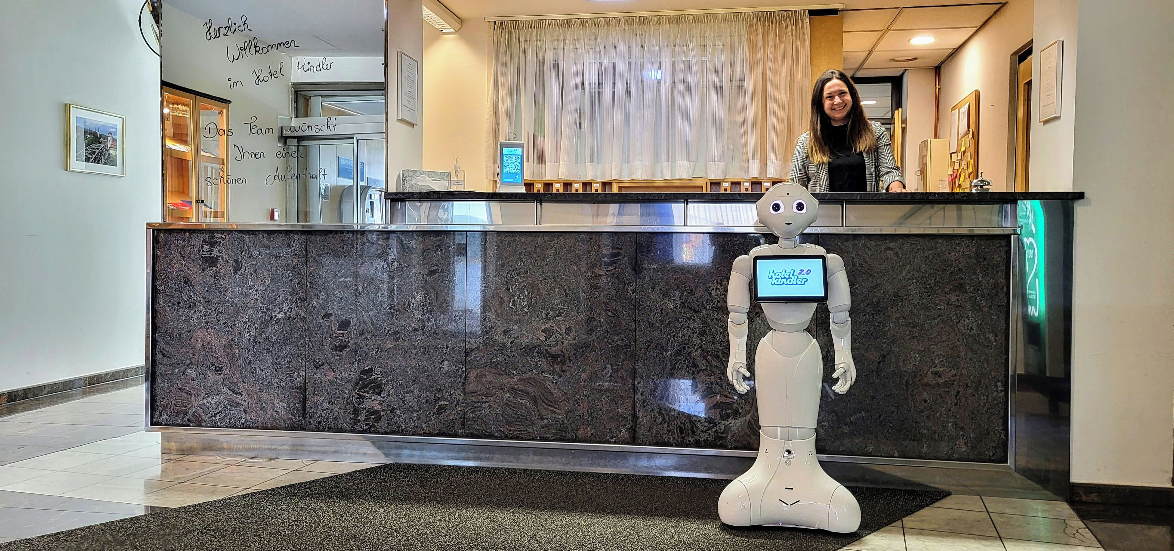 A reception area with a robot, a counter, and a woman behind it.