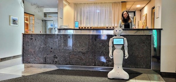 Zona de recepción con un robot, una barra de atención y una mujer detrás.