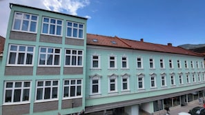 Un edifici de diverses plantes amb façana de color verd clar, nombroses finestres i teulada de teules vermelles.