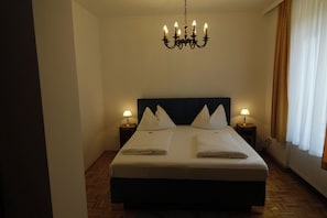 Habitació d'hotel amb un llit gran, dues taules de nit amb lampades, un penjóll i una finestra amb cortines.