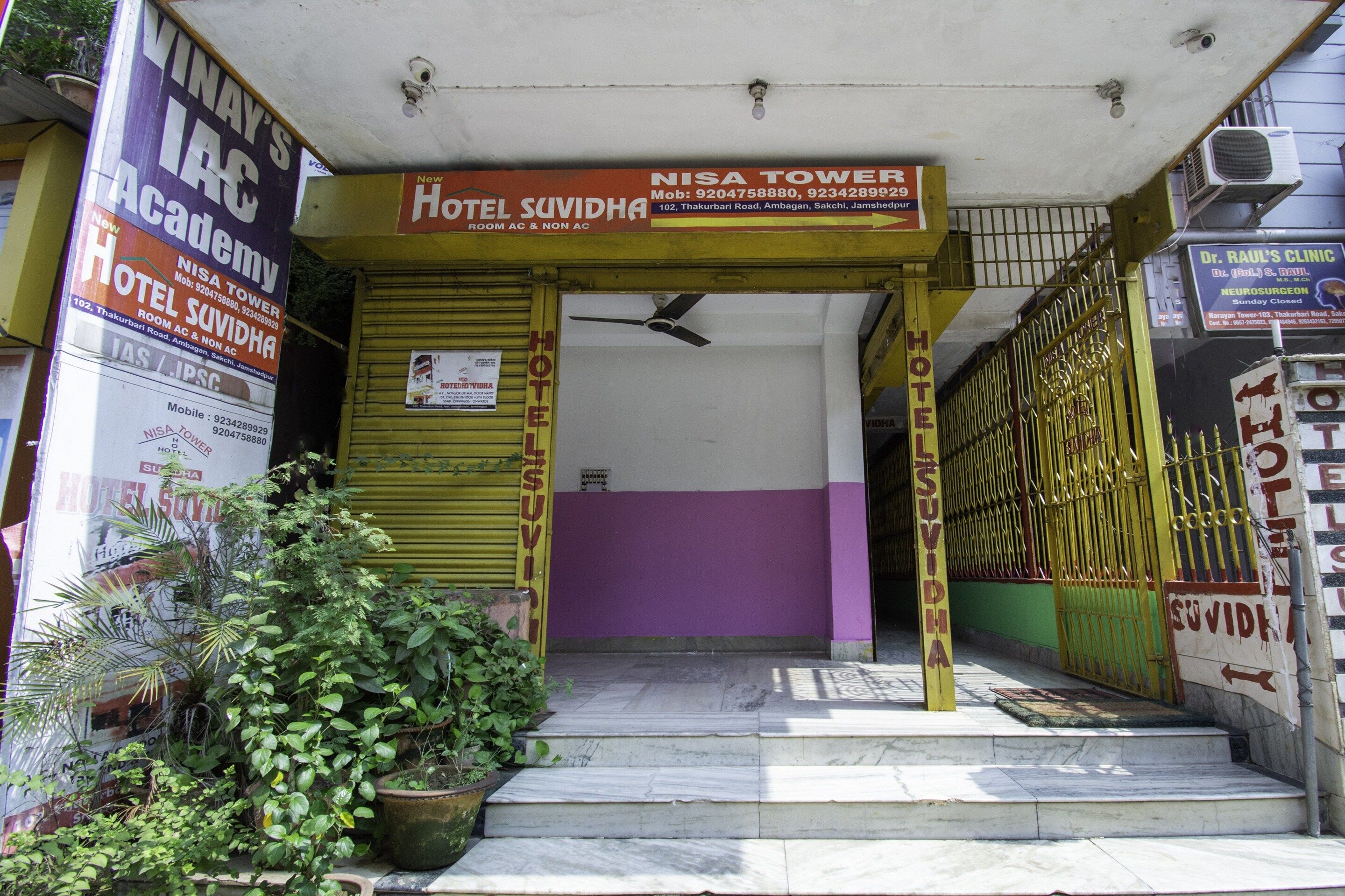 The entrance to a hotel with a purple and yellow facade, a staircase leading to the entrance, and multiple signs advertising the hotel and its services.