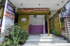 La entrada de un hotel con fachada morada y amarilla, una escalera que conduce a la entrada, y varios letreros que publicitan el hotel y sus servicios.