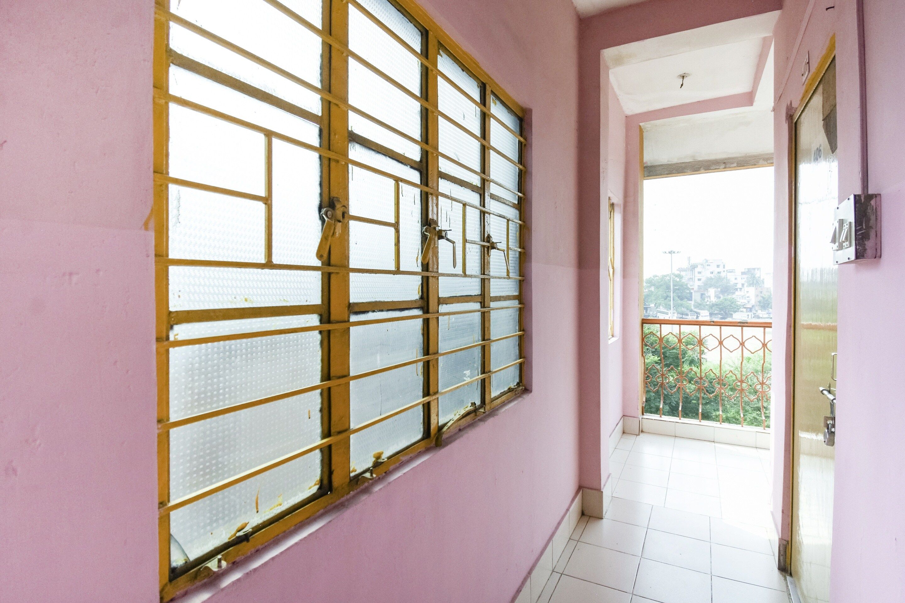 A corridor with a large window with metal bars, a balcony with a metal railing, and a door with a light switch on the wall.
