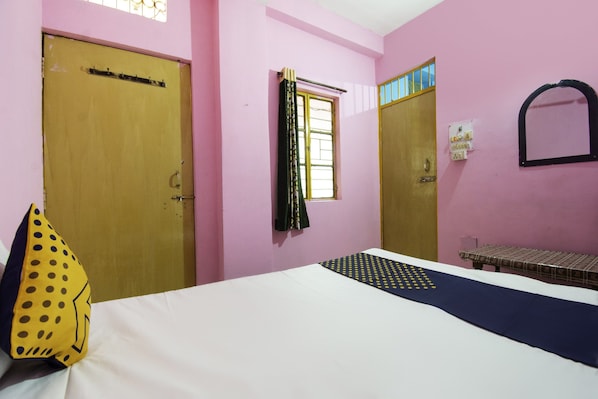 Una habitación con dos puertas, una ventana con cortinas, una cama con colcha estampada y una mesita con mantel decorado.