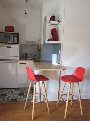 A compact kitchen with a microwave, a sink, and a small refrigerator. There are two red chairs at a wooden table. - New Listing (REIMS)